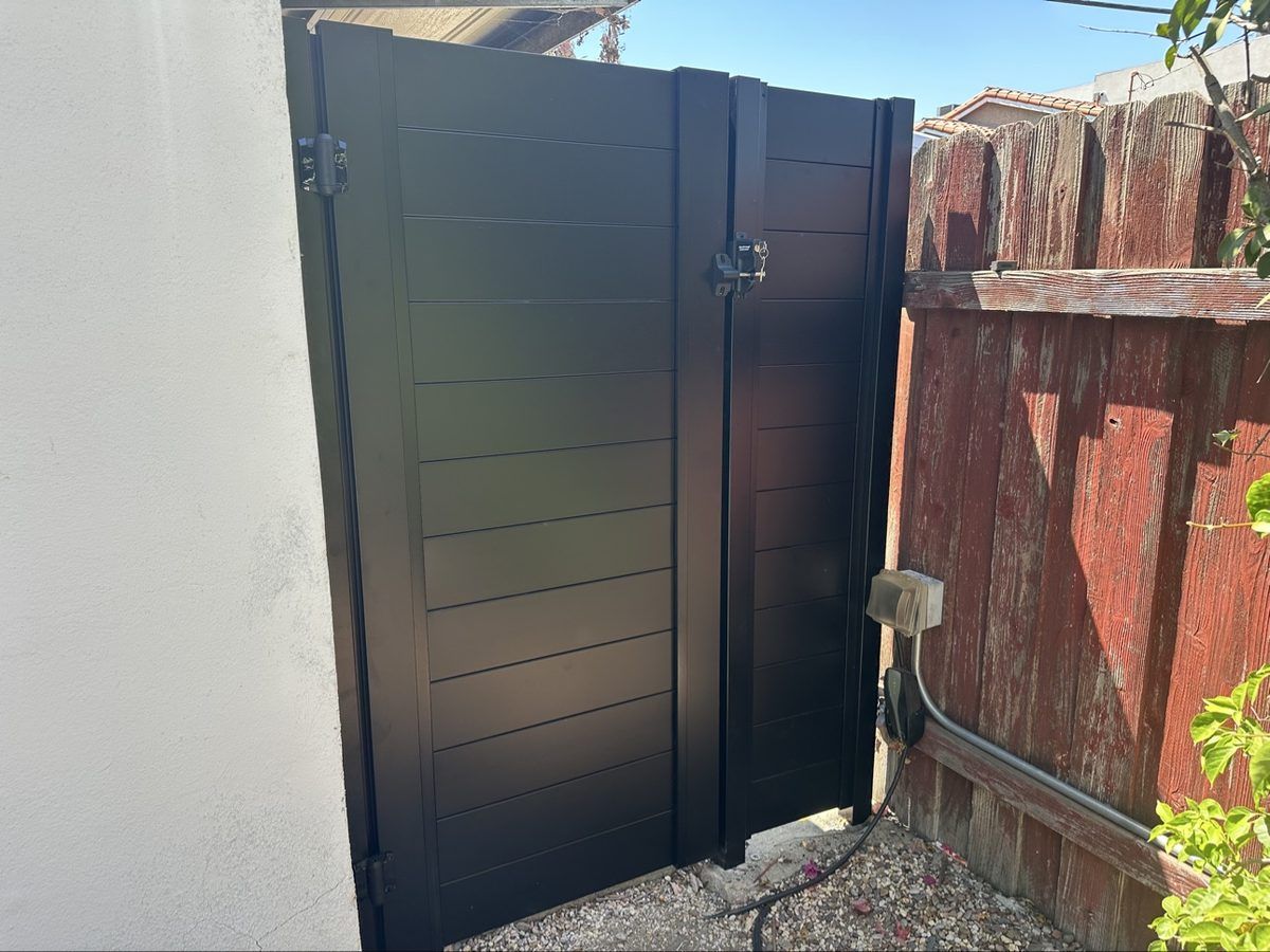 Black horizontal-slat aluminum gate with lock hardware beside an existing wood fence