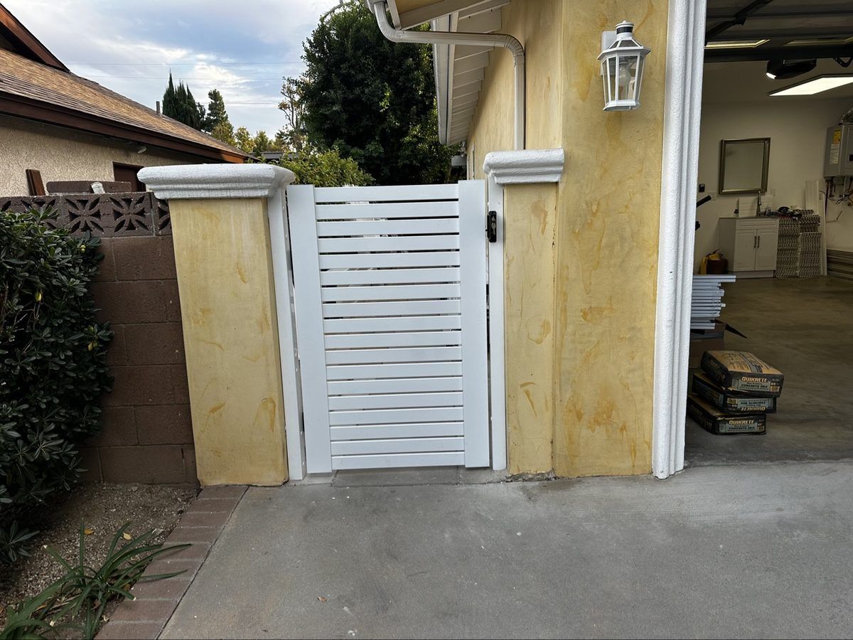 White aluminum pedestrian gate with horizontal slats between stucco pillars