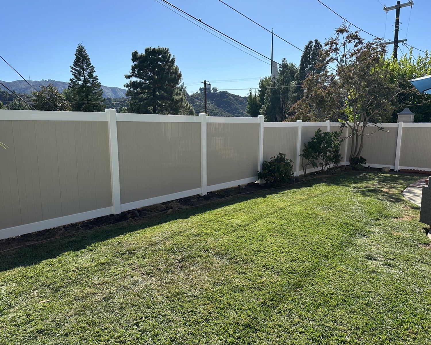 Tan vinyl privacy fence in a landscaped backyard