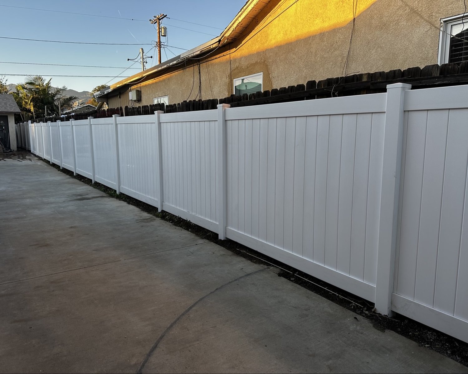 White vinyl privacy fence along a driveway at sunset