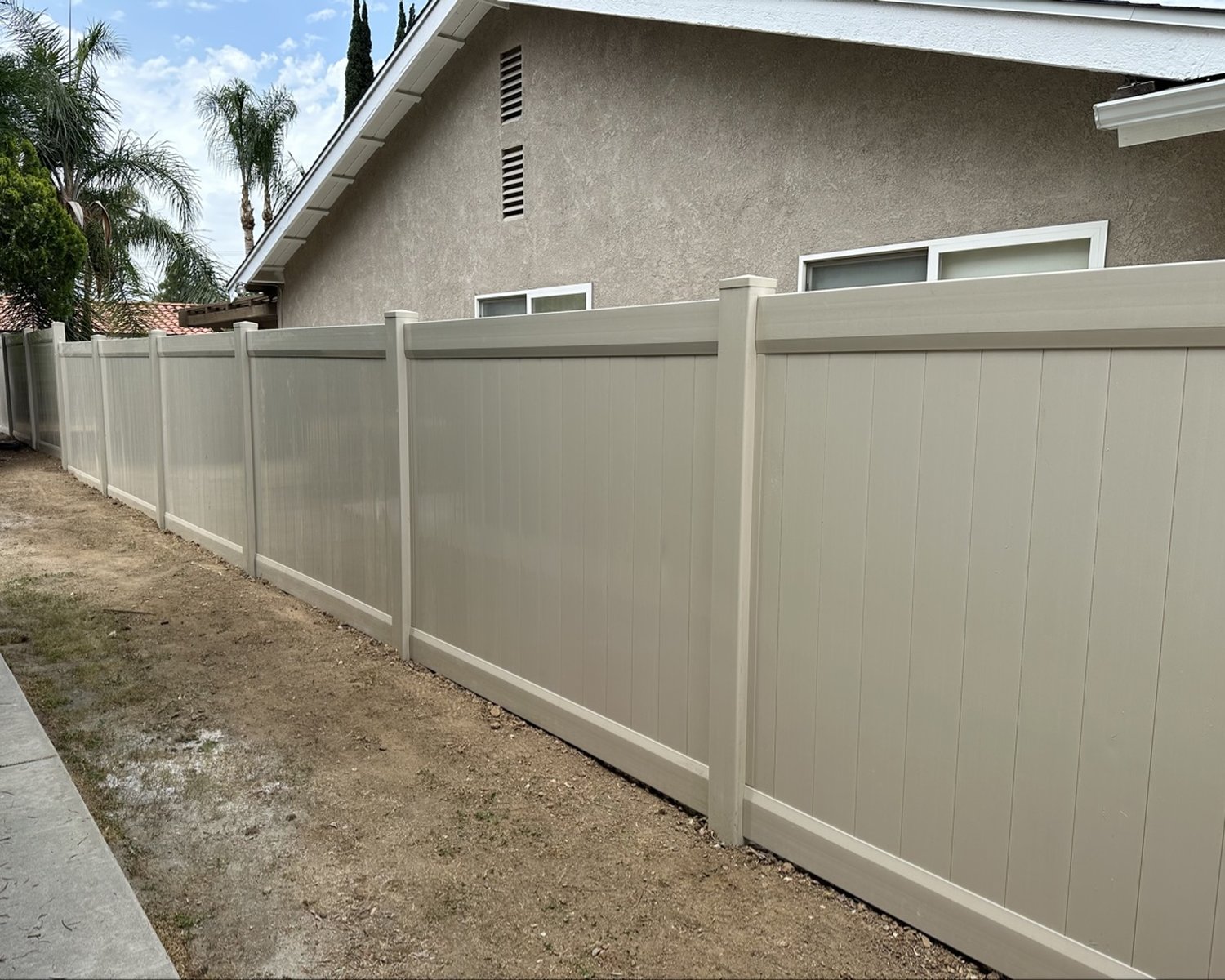 Long tan vinyl privacy fence run beside a house