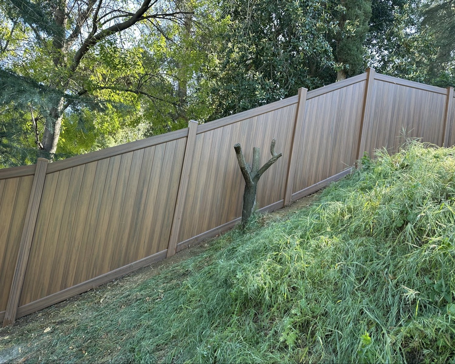 Wood-grain vinyl privacy fence on a hillside