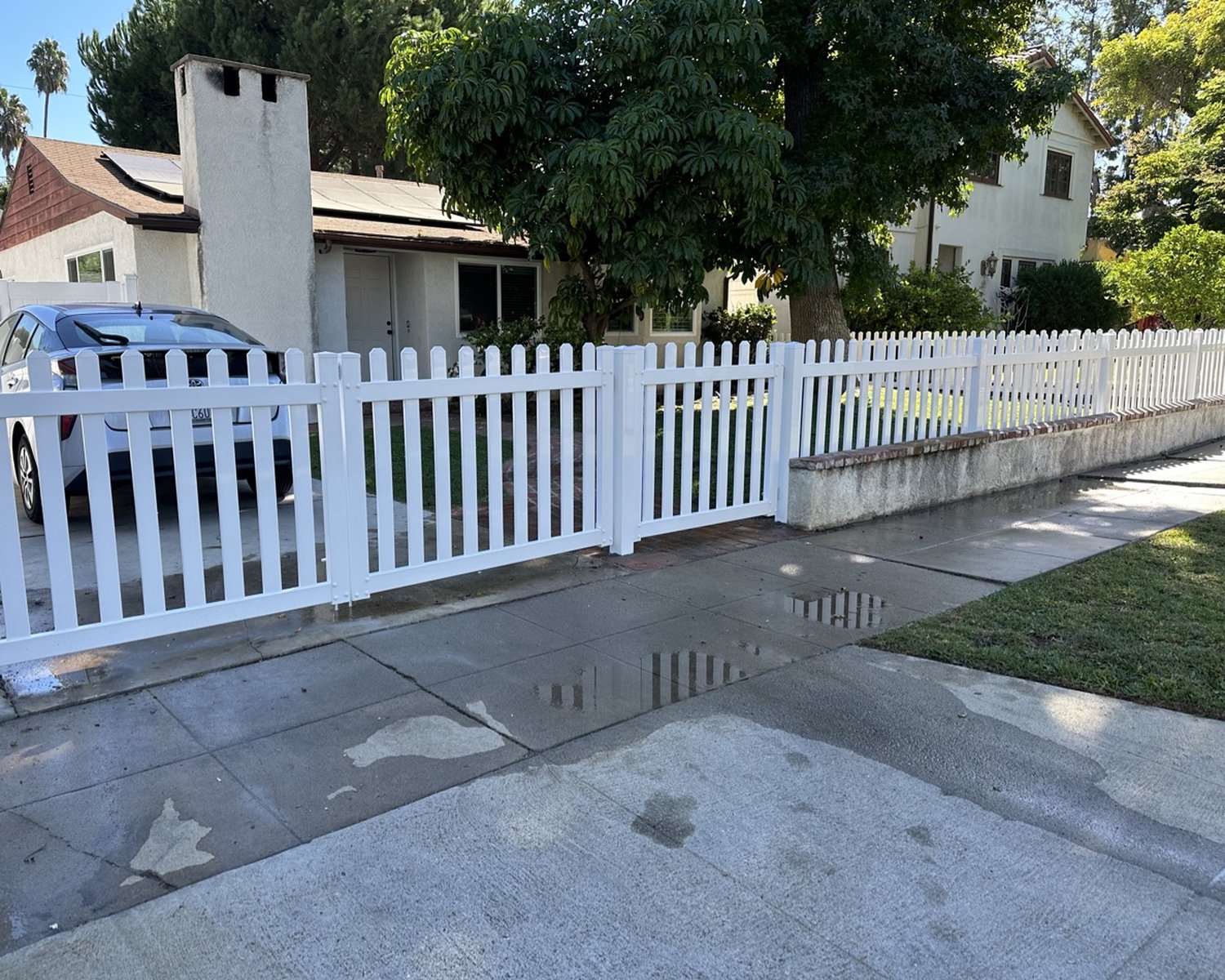 White vinyl picket double driveway gate in front of a house