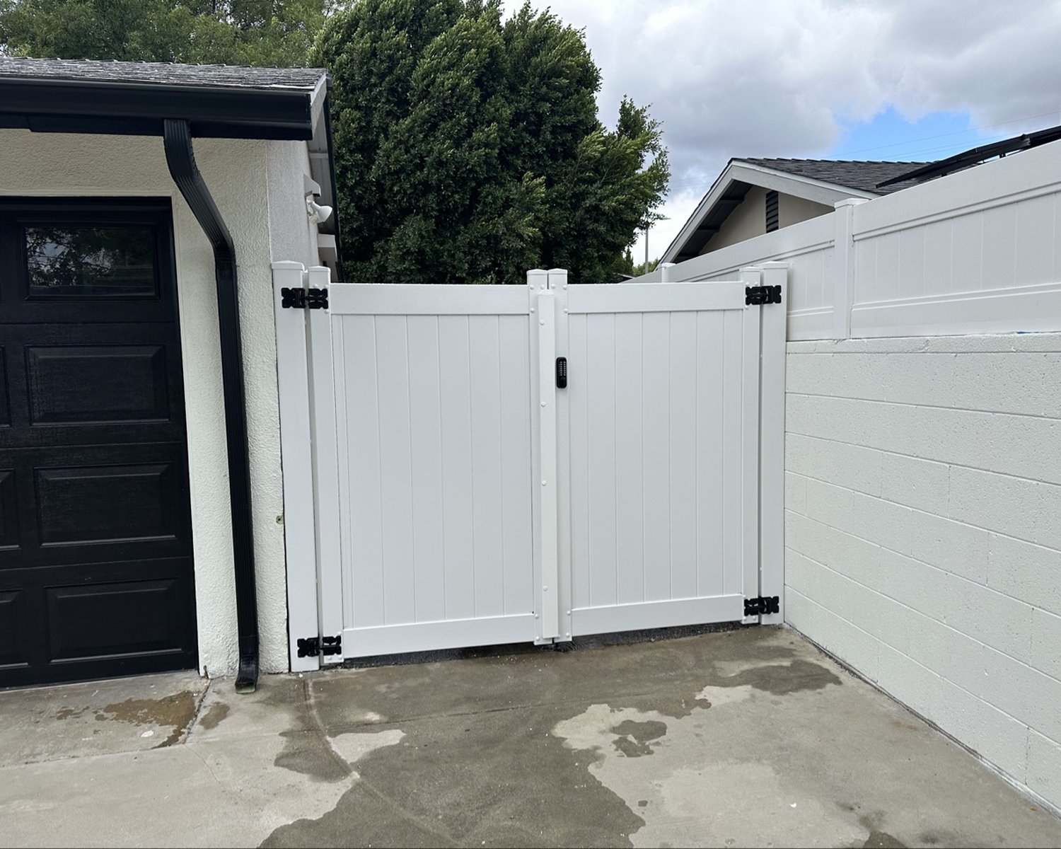 White vinyl double gate with black hinges by a garage