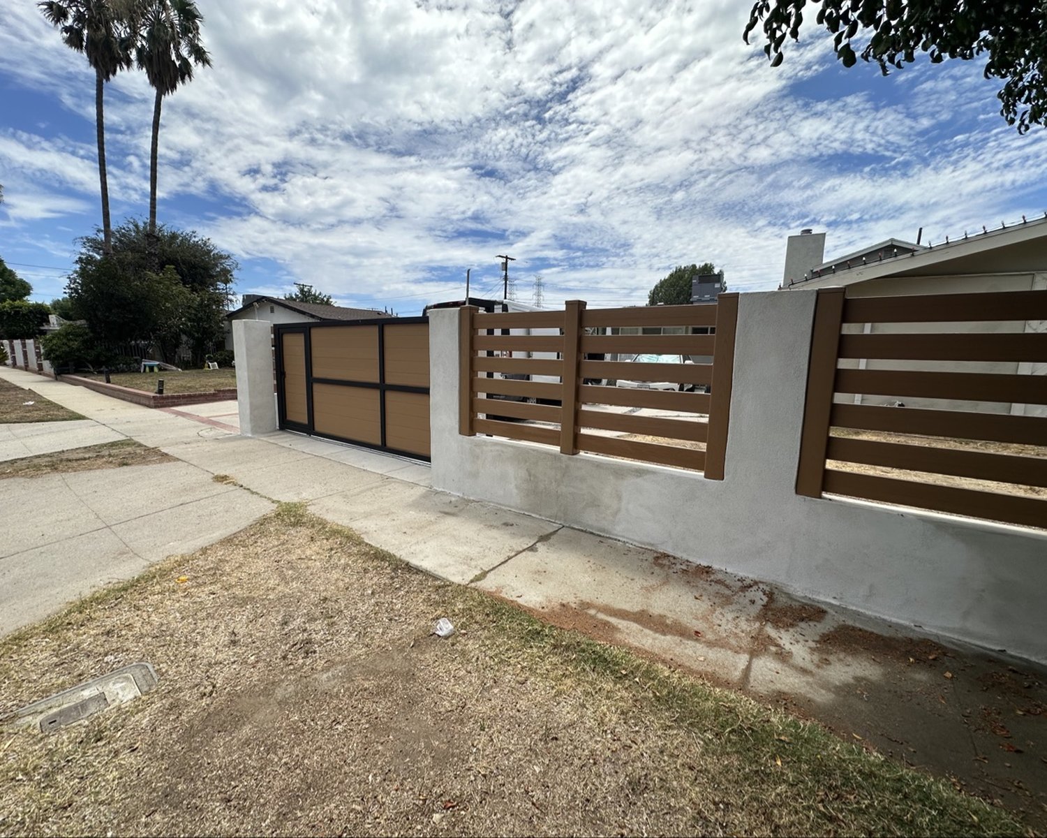 Wood-look fence with sliding gate between stucco pillars