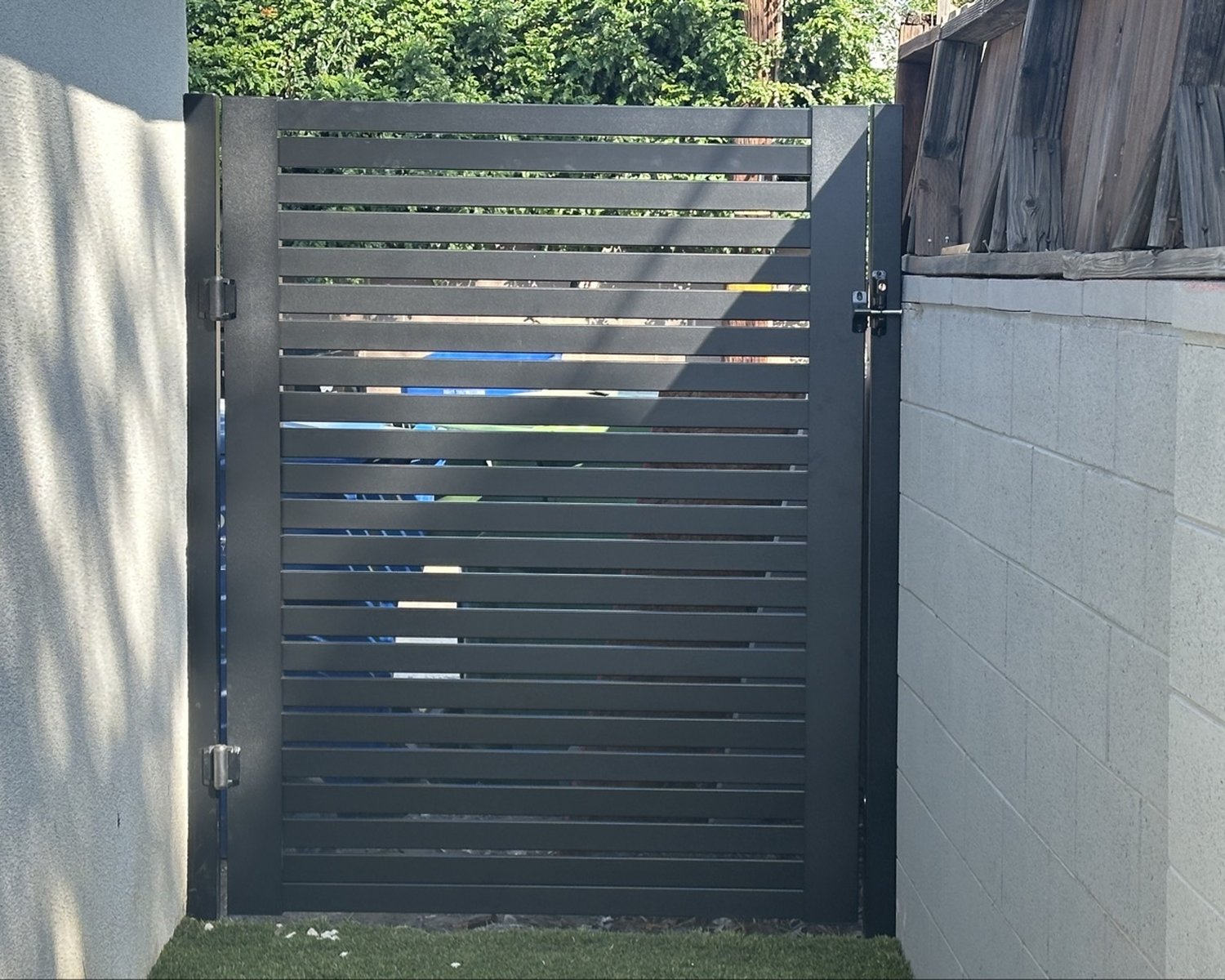 Black horizontal-slat gate between stucco and block walls